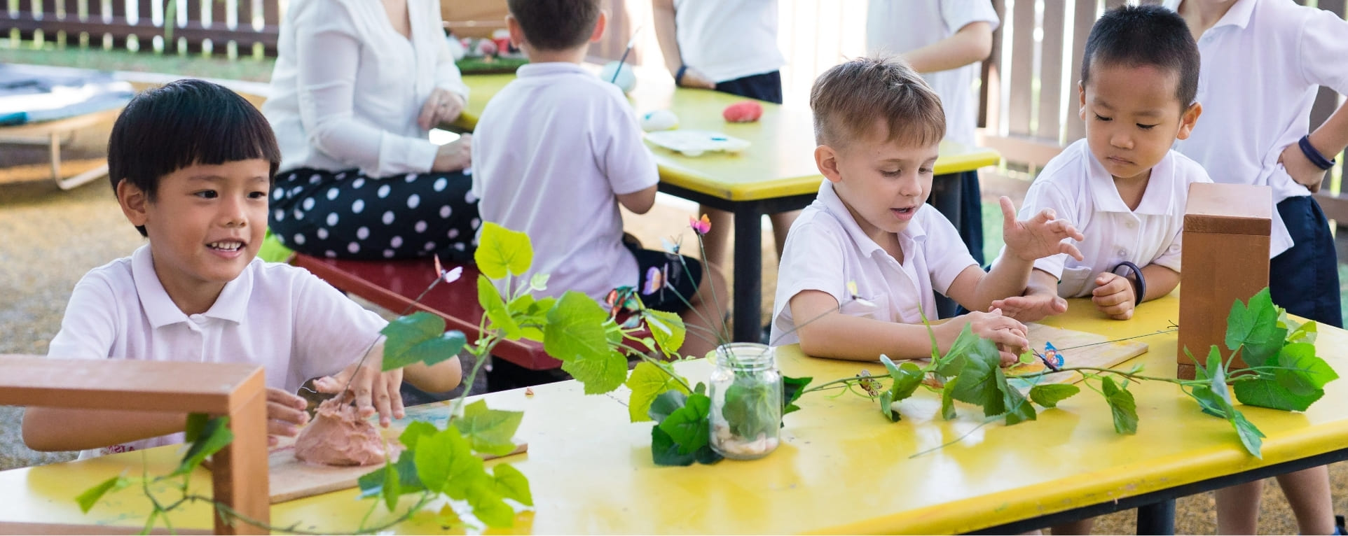AISM students engaged in a extracurricular activity at a table adorned with various plants and leaves, fostering exploration and learning.
