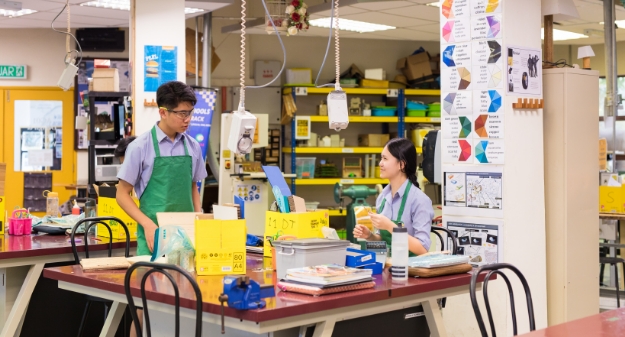 Two AISM students in a factory-like environment, focused on engineering and robotics.